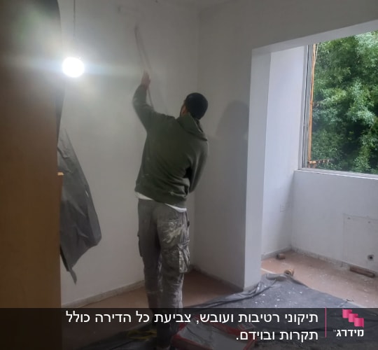 אדם צובע קיר עם רולר בחדר